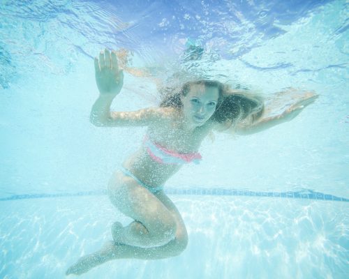 Beautiful young woman swimming underwater in pool